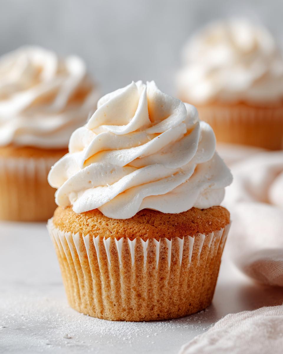Close-up of a delicious Champagne Cupcake topped with swirls of creamy buttercream frosting. Other cupcakes are blurred in the background.